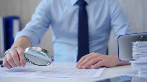 istock Businessman is carefully examining financial documents with a magnifying glass, highlighting the importance of thorough analysis in business. Audit and taxes 2164201858