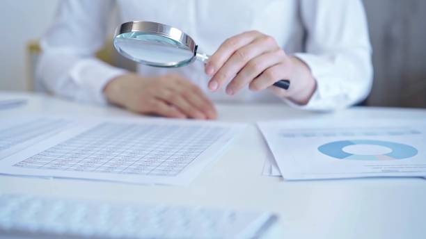 istock Businesswoman with white blues is analyzing financial data on a spreadsheet using a magnifying glass. Audit and taxes 2164201903