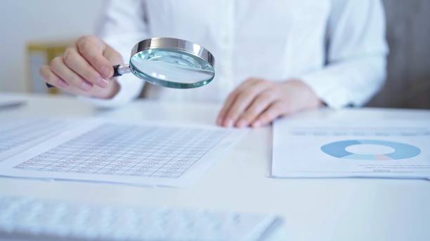 istock Businesswoman with white blues is analyzing financial data on a spreadsheet using a magnifying glass. Audit and taxes 2164201923