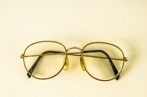 A pair of glasses with yellow lenses sits on a white surface. The glasses are old and worn, with a yellow tint that makes them appear slightly blurry. Concept of nostalgia and a connection to the past