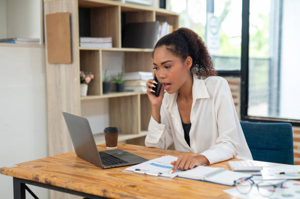 istock Young professional woman engaged in a phone conversation while working on her laptop at an organized office desk. 2164218549