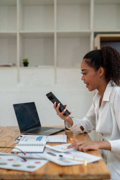 istock Young professional woman engaged in a phone conversation while working on her laptop at an organized office desk. 2164218644