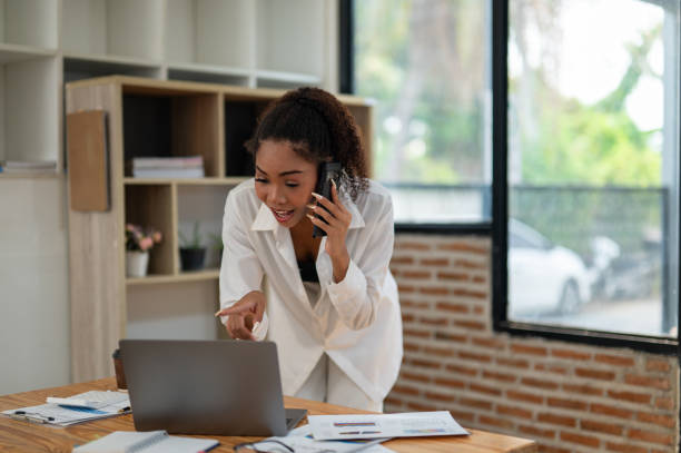 istock Young professional woman engaged in a phone conversation while working on her laptop at an organized office desk. 2164221342