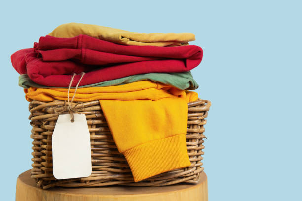 Colorful folded clean clothes in a wicker basket with a blank price tag, suggesting a clothing sale or retail stock.