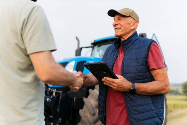 istock Happy elderly farmer with digital tablet shaking hands with a man on the farm 2164243272