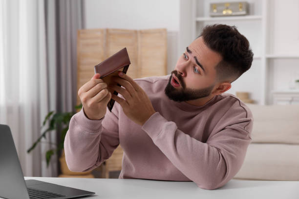istock Confused man with empty wallet at white table indoors 2164250692