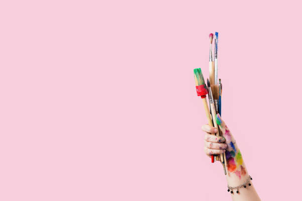 istock A hand holding paintbrushes against a pink background, symbolizing artistic expression 2164250834