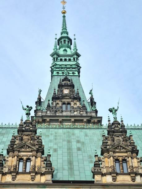 Copenhagen, Denmark: view of the main clock face on the tower of Copenhagen City Hall (Københavns Rådhus) in Denmark. The clock is set within the massive red brick tower, which stands at 105.6 meters (346 feet), making it one of the tallest structures in Copenhagen. Designed by architect Martin Nyrop and completed in 1905, the National Romantic style tower features intricate ornamental details. The clock face itself is characterized by a large, gilded design with Roman numerals and ornate hands, framed by decorative architectural elements and a small balcony. It serves as the primary timekeeper for Rådhuspladsen (City Hall Square) and remains a central landmark of the Danish capital.