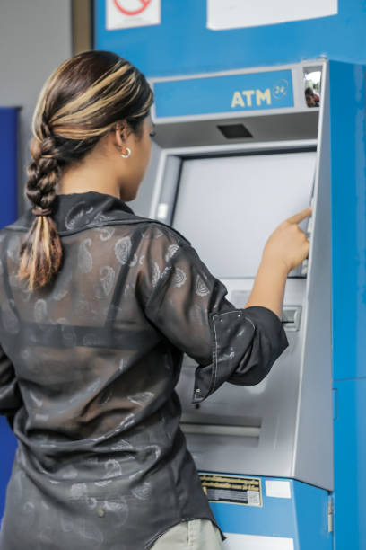 istock young woman withdrawing money with credit card from ATM machine typing pin code 2164258702