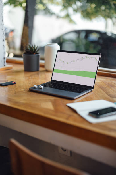 A cozy cafe scene with a laptop displaying a graph, a notepad, and a phone on a wooden table by the window.