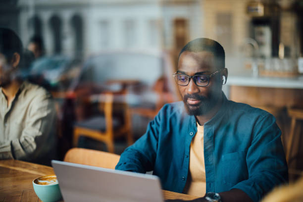 istock Man Working on Laptop in Cafe Viewed Through Window 2164260763