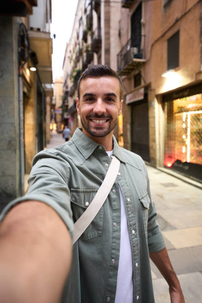 Young adult happy Caucasian man taking smiling selfie on Madrid touristic city street in background. Vertical young happy Caucasian man taking smiling selfie on Madrid touristic city street in background. Millennial handsome tourist takes lighthearted photo outdoors on his vacation trip in Europe selfie madrid photos stock pictures, royalty-free photos & images