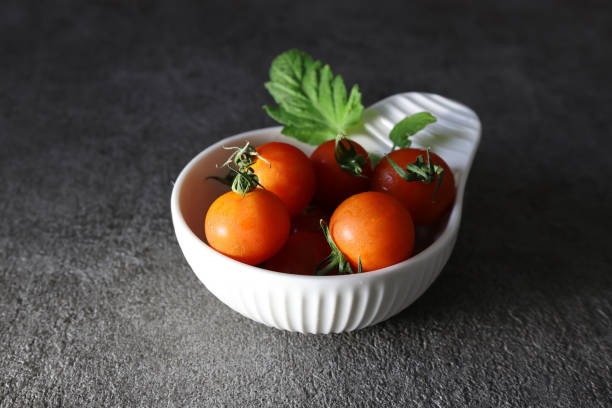 Cherry tomatoes in a white pottery bowl isolated on a gray background.