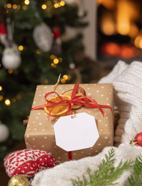 istock Gift tag on a present near sweater against Christmas tree lights and burning fireplace, mockup 2164276157