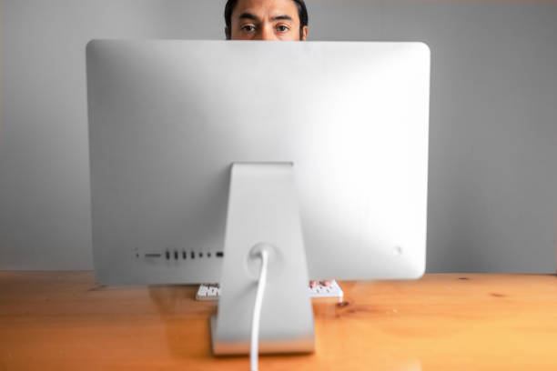 Back of a computer and a person peering over it. Concept of the burden of technology on humanity