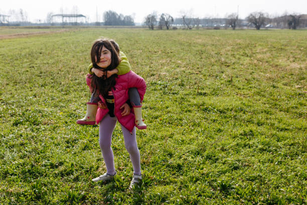 elder girl watching camera with smaller child on her back doing piggyback ride outside