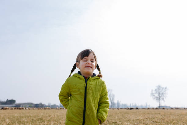 small girl with braids in green jacket smiling with closed eyes