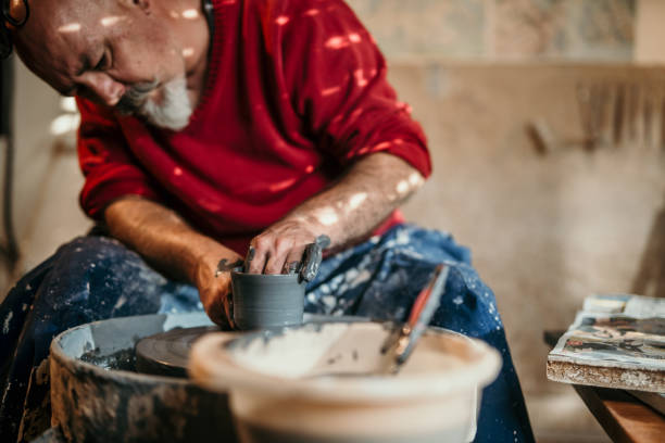 Close-up of an artist's hands shaping clay and using a sculpting tool on a pottery wheel. The image highlights the intricate and creative process of handmade pottery in a studio environment.