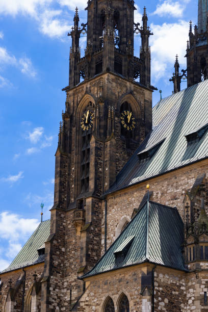 Tall red brick tower of Saint James Church in Chelmno with a pointed spire and cross against a bright sky.