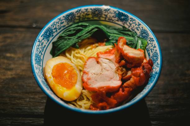 Chinese Fried Noodles with Toppings Chinese fried noodles in a bowl with Char Siu, hard-boiled egg, and a vegetable on a wooden table. Cantonese cuisine with Kopitiam style. Top view angle with the object at the center. kopitiam egg stock pictures, royalty-free photos & images