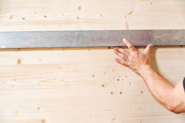 Carpenter is installing a wooden plank on a wall using a spirit level in his workshop, ensuring accuracy and precision in his work
