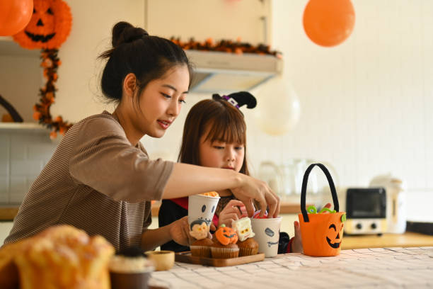 istock Smiling young mother and her little daughter making Halloween cupcakes in kitchen, getting ready for the holiday 2164305907