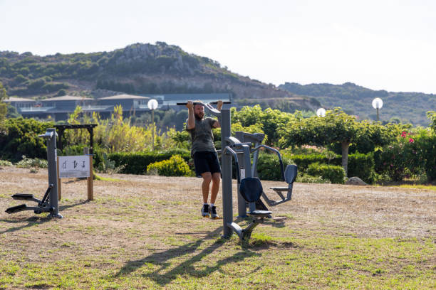 A man performs pull-ups on outdoor gym equipment, surrounded by lush greenery and mountains. The image captures a workout in a serene, natural environment.