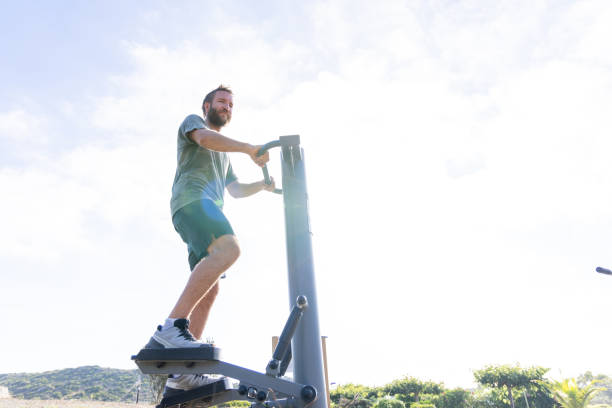 A man works out on a stepper machine at an outdoor gym, enjoying the open air and natural surroundings. The image highlights a healthy and active lifestyle in a scenic environment.