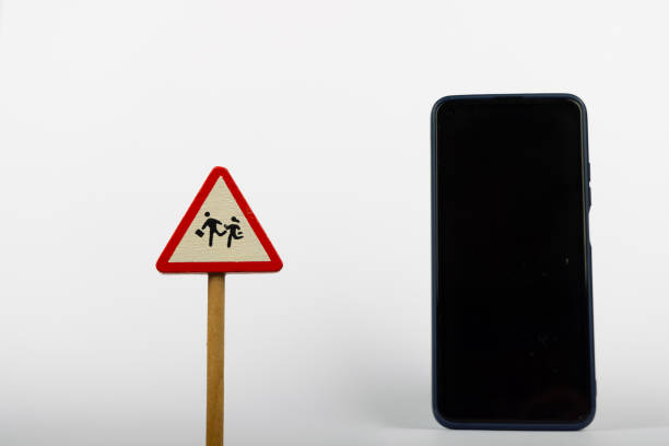 A wooden toy warning sign labeled WARNINGS CHILDS is placed next to a smartphone on a clean white background, highlighting safety and technology