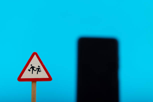 A toy wooden warning sign reading Danger Children is shown with a blurred smartphone in the background, on a blue backdrop, creating a conceptual image