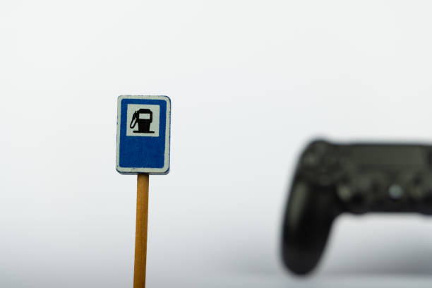 A wooden toy gas station stands out in clear focus, with a game controller blurred artistically in the background, against a simple white background