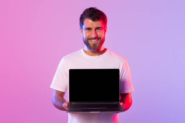 istock Young Man Holding Laptop in Studio With Colorful Lighting 2164328209