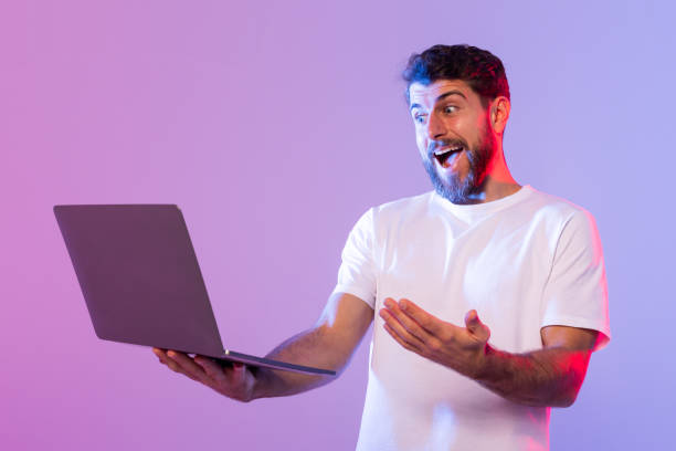istock Young Man Surprised While Using Laptop Against Purple Background 2164328223
