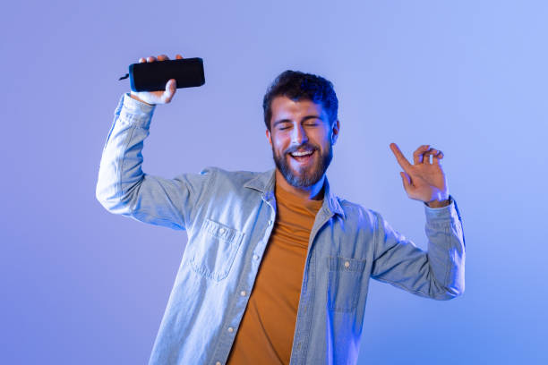istock Young Man Dancing Joyfully Indoors at Night With Bluetooth Speaker 2164328259