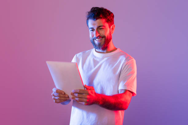 istock Man in White T-Shirt Holding Tablet in Neon Light 2164328265