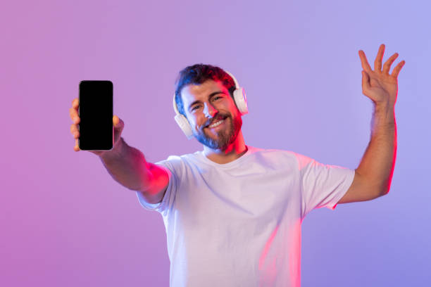 istock Man Wearing Headphones Holding Cell Phone With Black Screen 2164328297
