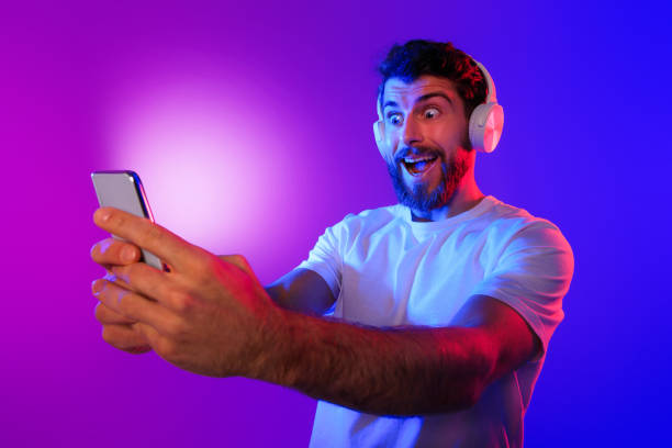 istock Surprised Guy Wearing Wireless Headphones Looks At Mobile Phone, Studio 2164328314