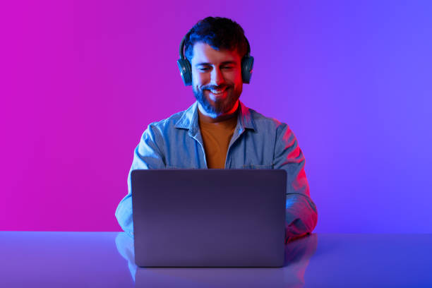 istock Happy Millennial Guy Wearing Headphones Browsing Internet On Laptop, Studio 2164328319