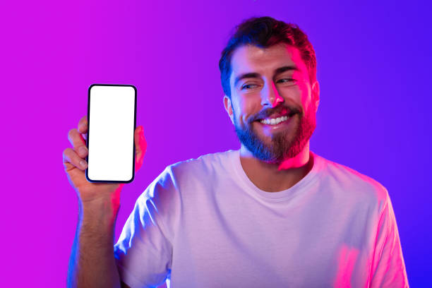 istock Cheerful bearded young man showcasing smartphone mockup screen, neon studio 2164328347