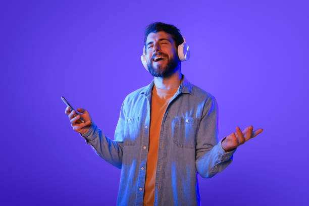 istock guy holds phone singing enjoying music through wireless earphones, studio 2164328371