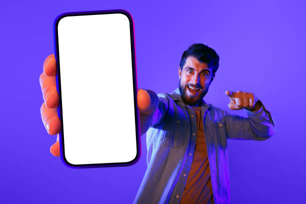 istock guy pointing to camera showing blank screen of smartphone, studio 2164328377