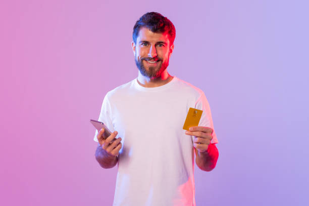 istock Man Holding Smart Phone and Credit Card in Neon Light 2164329010