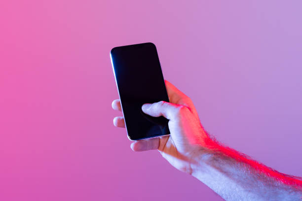 istock Hand Holding Smartphone Against Purple Background During Evening 2164329013