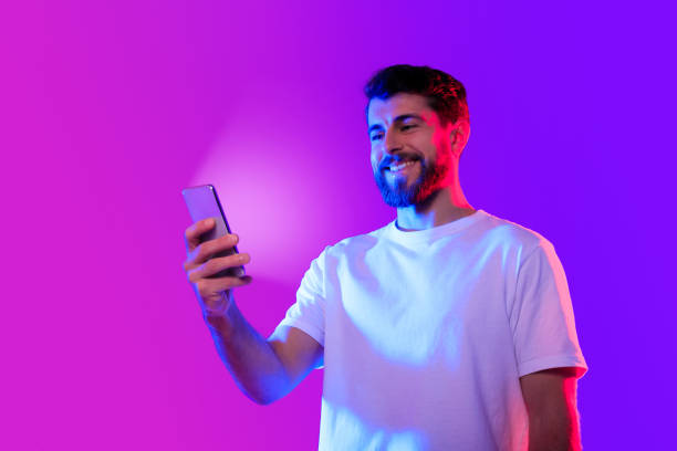 istock Cheerful caucasian man scrolling through a smartphone app, neon background 2164329017