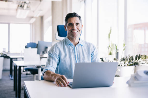 istock Businessman looking at the camera with a smile, while working at the office with a laptop 2164330746