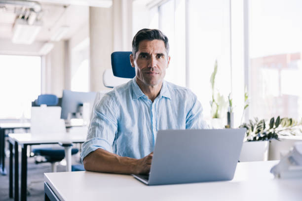 istock Businessman looking at the camera with a positive emotion, while working at the office with a laptop 2164330761