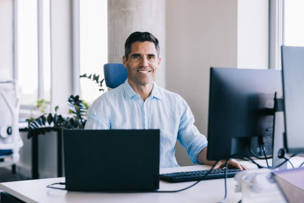 istock Businessman looking at the camera with a smile, while working at the office with a laptop 2164330776