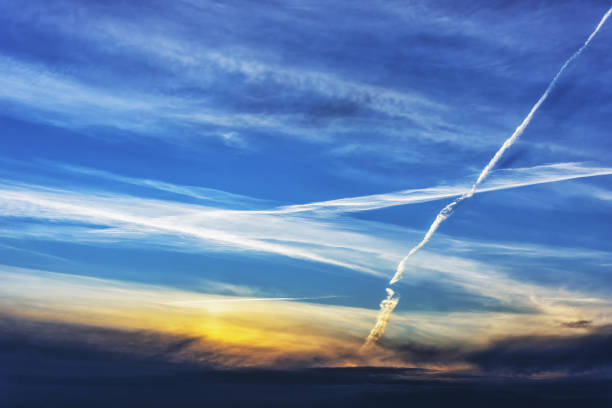 White airplane tracks in the blue evening sky with clouds