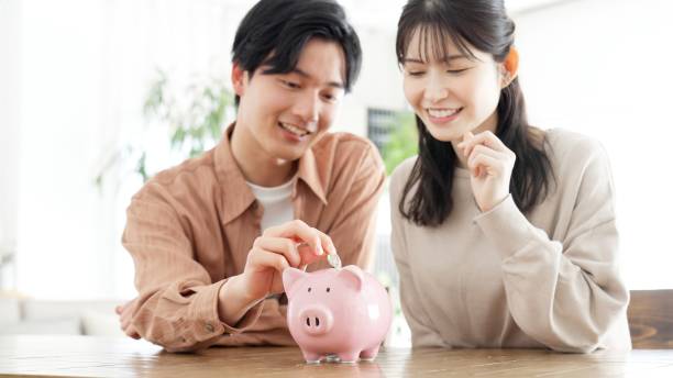 couple putting money into a piggy bank - お金 ストックフォトと画像