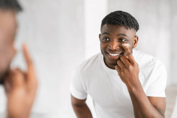 istock Cheerful millennial black guy applying moisturizer on face in bathroom 2164336459